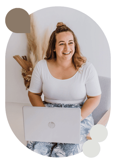 Smiling woman with a laptop, sitting indoors in a well-lit room with decorative plants in the background.